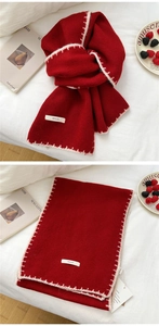 Detail of red knit scarf featuring white stitched edges and brand woven label