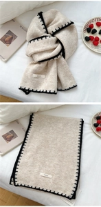 Detail of cream knit scarf with contrast black stitching and woven brand label