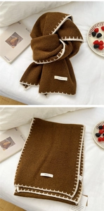 Detailed knit texture of thick dark brown winter scarf with white edge stitching and label