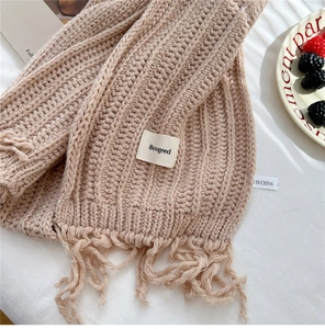 Detail of beige knit scarf with tassels and brand label on cozy textured surface