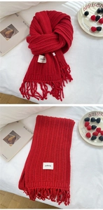 Detail of red knitted scarf with fringe, thick wave texture, and minimalist logo tag