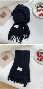 Detailed view of black ribbed knit scarf with tassel fringe and white logo tag