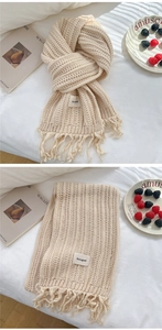 Detail of cream chunky knit scarf featuring vertical ribbed texture and fringe tassels