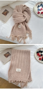 Close-up of soft pink chunky knit scarf with fringes and woven brand label on fabric