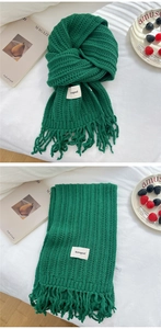 Close-up of dark green chunky knit scarf with fringe and a white fabric label