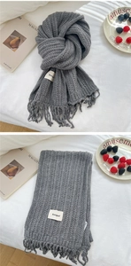 Detail of grey knitted winter scarf featuring fringe edges and decorative label