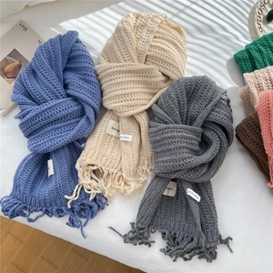 Knitted tassel scarves in blue, beige, and grey colors on a minimalist white background