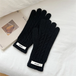 Primer plano de guantes de punto trenzado negros con etiqueta tejida sobre tela blanca