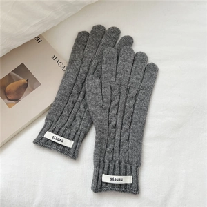 Detalle de guantes de punto trenzado gris oscuro con etiqueta de marca sobre tela blanca