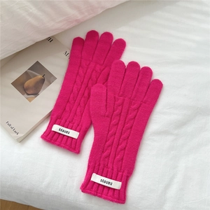 Detalle de guantes de punto trenzado rosa con etiqueta blanca sobre una tela blanca suave