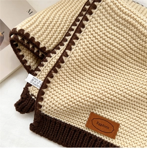 Detail of warm knit scarf showing cream texture, brown crochet edge and leather brand tag