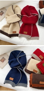Detail of color-block knitted scarf texture and premium leather brand label on bed