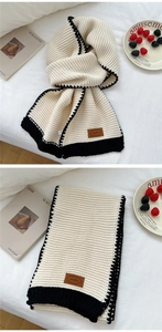 Detail of a beige knitted scarf with black ribbed edges and brown leather brand patch