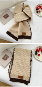 Detailed close-up of chunky knit scarf showing beige wool texture and brown leather label