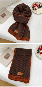Detail of chunky knit scarf in brown and orange with leather tag on cozy bedding