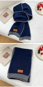 Close-up of thick navy and grey knit scarf with textured ribs and orange leather patch