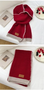 Detail of red knit scarf featuring contrast beige ribbed edges and brown leather patch label