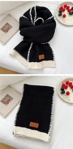 Close-up of thick black knit scarf with white stitched edges and leather logo patch detail