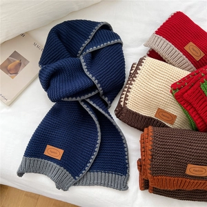 Chunky knit two-tone winter scarf with leather label on soft white fabric background