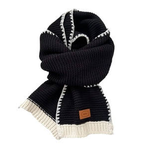 Two-tone chunky knit scarf in black and beige with a leather logo patch for winter warmth
