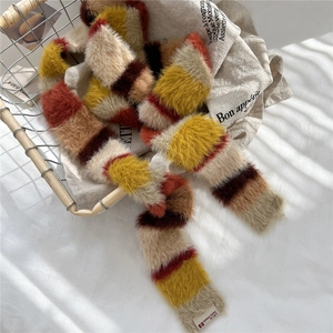 Macro detail of soft striped faux fur scarf in warm yellow and orange tones on a linen cloth