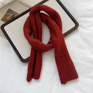 Detail of red knitted scarf with ribbed ends on a white fabric background with magazine