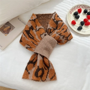 Flat lay of a leopard print knitted scarf with a cross-loop design on a white fabric surface