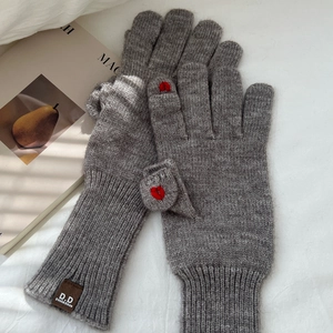 Dettaglio di guanti in maglia grigi con ricamo a cuore rosso ed etichetta del marchio