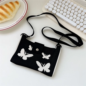 Detail of black knitted crossbody bag with white butterfly pattern on a white desk