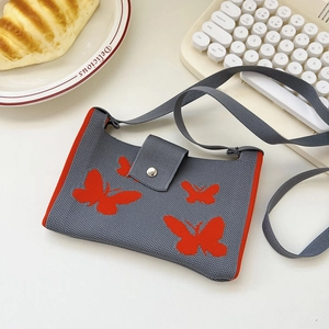 Detail shot of grey knitted crossbody bag featuring orange butterfly patterns and magnetic buckle