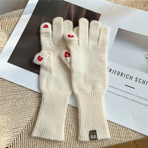 Dettaglio di guanti in maglia beige con ricamo a cuore rosso ed etichetta del marchio in cuoio