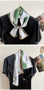 Detail of silk satin scarf featuring crane prints and green strokes tied on a black dress