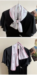 Close-up of floral grey silk scarf with pink edges tied on elegant black silk fabric
