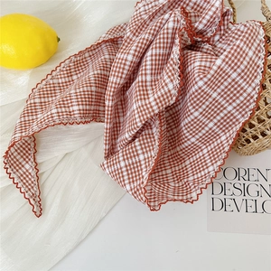 Détail d'un foulard en coton vichy rouge avec bordure en dentelle sur fond décoratif