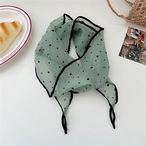 Detail of light green polka dot gauze scarf with black trim on a white surface