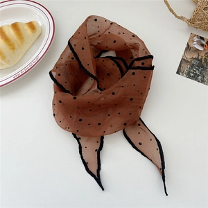 Close-up of a sheer brown polka dot scarf styled on a white table with brunch props