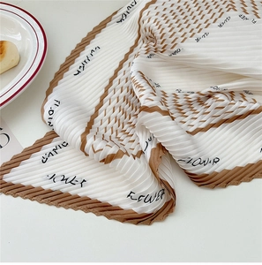 Macro detail of pleated pearl white silk scarf with brown geometric flower print