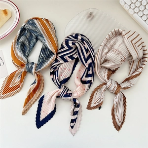 Three pleated patterned scarves with paisley and geometric prints on a minimalist desk