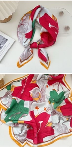 Detail of square floral silk scarf with red and green lily patterns and orange borders