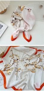 Detail showing elegant white floral silk scarf with orange borders and satin texture