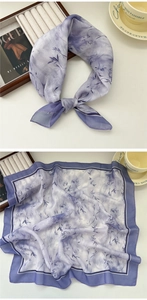 Close-up of a purple square scarf with floral leaf patterns on an elegant wooden tabletop