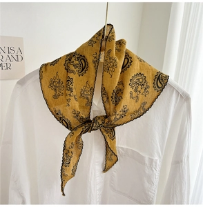 Detail of ginger yellow paisley silk scarf with black embroidery wavy edges on white shirt
