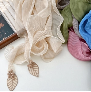 Détail d'une écharpe en mousseline plissée avec broderies de feuilles et pompons