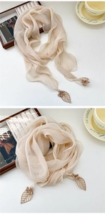 Détail de l'écharpe en mousseline plissée beige avec broderie feuille et pompons