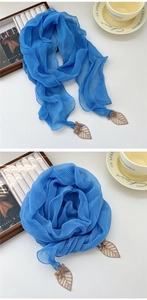 Détail d'un foulard en soie plissé bleu roi avec pendentifs feuilles et glands