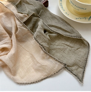 Detail of two-tone linen scarf with white crochet edge next to a coffee cup