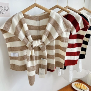Striped knit shawl set in khaki, red, and black, hanging on wooden hangers in a cozy room