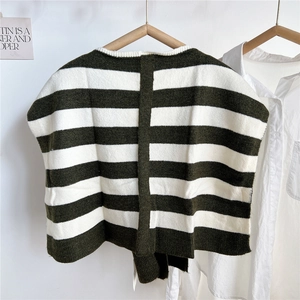 Detail of green and white striped knit shawl vest on a wooden hanger against white wall