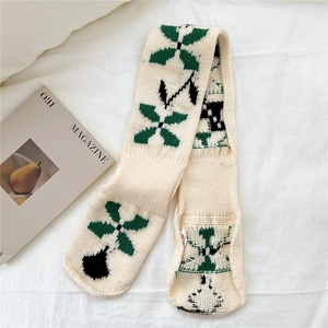 Close-up of thick knit beige scarf with green floral geometric patterns on soft fabric