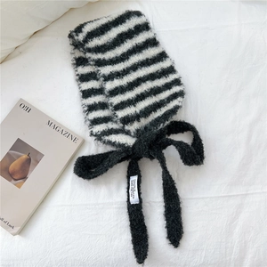 Détail de l'écharpe rayée en tricot avec un nœud noir pelucheux et une étiquette blanche